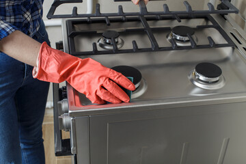 modern gas oven. a girl in red rubber gloves washes a gas stove with a sponge. girl in jeans and a blue plaid shirt. Cleaning in the kitchen.