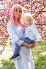 Beautiful woman with little baby boy near pink sakura blooming tree. Spring concept