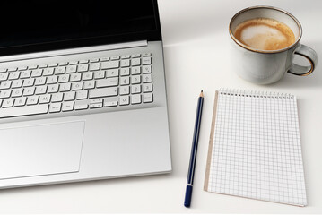 laptop computer and note pad on white office desk with cup of coffee