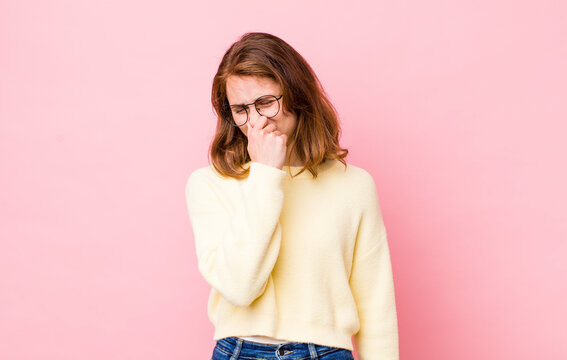 young pretty woman feeling disgusted, holding nose to avoid smelling a foul and unpleasant stench