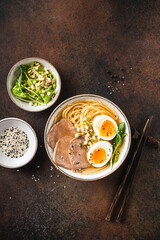 Ramen soup noodle bowl with egg and meat on dark brown background, table top view. Asian cuisine food