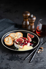 Baked camembert or brie cheese with cranberry sauce and fresh figs on a black plate, closeup view