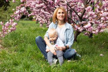 Naklejka na ściany i meble happy mother in a blue shirt sitting with a baby son in spring. Motherhood and femininity