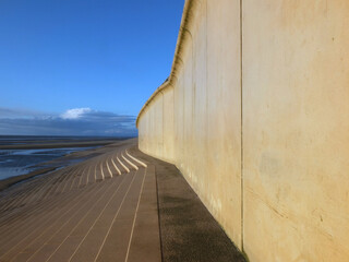 perspective view of the concrete seawall in blackpool with steps leading down to the beach in warm afternoon sunlight with blue cloudy sky