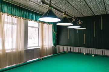Billiard table with green cloth. Billiard room. Board game. A lamp for lighting the billiard table in the billiard room.
