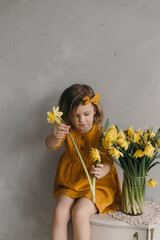 little girl in a yellow dress with a beautiful bow holds a narcissus flower