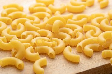 Close up uncooked elbow macaroni on wooden chopping board