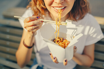 Young woman having a lunch break and eating wok noodles outdoors. Fastfood meal concept