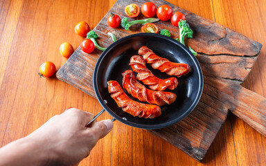 Fried sausage in a black pan in chef hands.