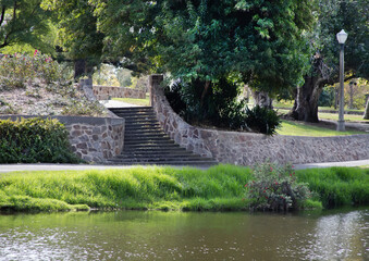 Summer landscape in the park with a stone staircase, path, river bank, green grass and trees