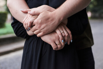 Close-up picture of romantic couple holding hands. A man is embracing a woman from behind. Romantic relationship concept. Mutual understanding in couple. Psychological issues and solving.