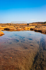 Fototapeta na wymiar dry river rock formation with water and vintage iron bridge and blue sky at morning