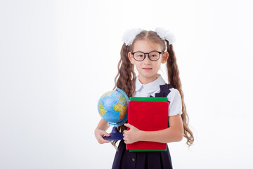 a little girl in glasses and a school uniform holds a book and a globe isolated on a white background