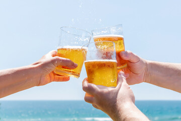 Three friends toasting with beer on a beach in front of the sea. Happy and fun summer