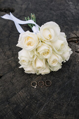 Wedding details.  Wedding rings with diamond and wedding bouquet of white roses on the wooden background. Close up