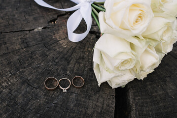 Wedding details. Wedding decor. Wedding rings and wedding bouquet of white roses on the wooden background.