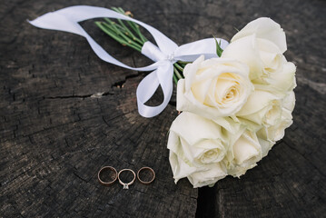 Wedding details. Wedding decor. Wedding rings with diamond and wedding bouquet of white roses on the wooden background.