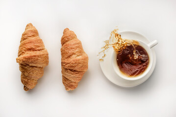 A cup of coffee and a couple of croissants on a white background.