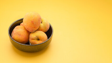 Fresh peaches fruit on a bowl over a yellow background