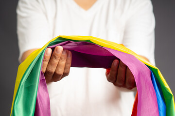Close-up of hand holding the rainbow flag or LGBT flag while standing on a gray background