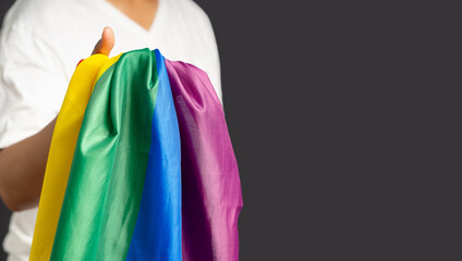 Close-up of hand holding the rainbow flag or LGBT flag while standing on a gray background
