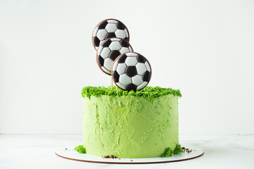 Birthday cake for a football fan with green cream cheese frosting, grass and soccer balls gingerbread cookies on top. White background