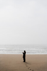 Fototapeta na wymiar someone walking alone on the beach on a foggy day with a mobile phone