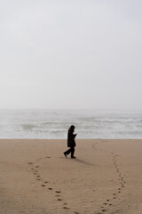 someone walking alone on the beach on a foggy day with a mobile phone