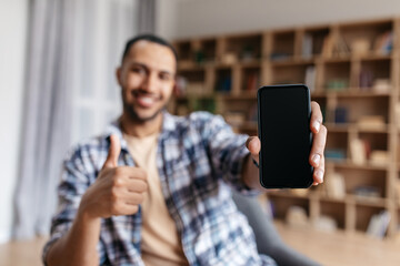 Recommendation. Happy arab guy holding smartphone with blank screen in hand and making thumb up gesture, mockup