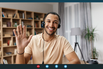 Videocall screenshot of cheerful arab man in headset having web conference, waving hand at camera...