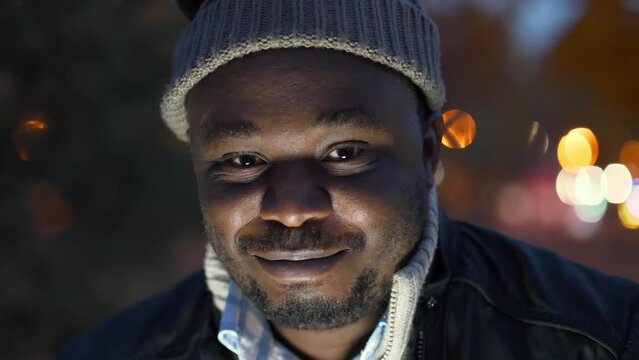 Cheerful african american man in winter hat looks at the camera and smiles shyly