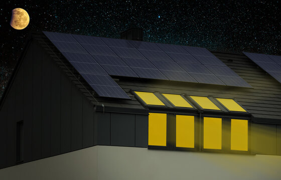 Solar Panels On Roof Of House At Night. Clean Energy Production. Light In Windows Of House. Conceptual Image.