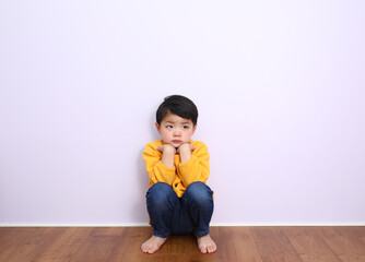 壁に泣きながら座り込んでいる男の子。悲しい表情。