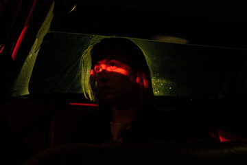 the model looks at the red light in the car, the dark time of the day, the night lights of the city.