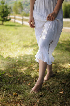 Close up of barefoot woman in white dress is walking on the grass