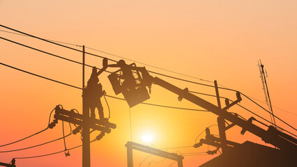 Silhouette workers installing electrical equipment on utility poles.