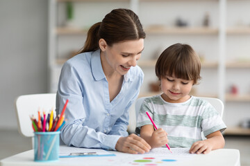Creativity lessons for children. Happy little boy drawing with professional woman teacher at classroom