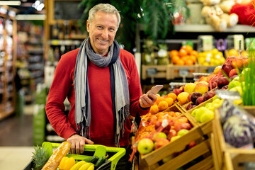 Portrait of cheerful senior man shopping at supermarket, holding smartphone