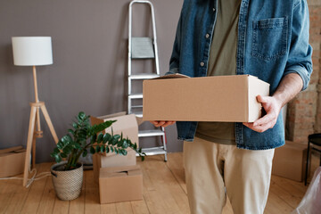 Horizontal shot of unrecognizable young man wearing casual clothes bringing boxes with things to new apartment © Mediaphotos