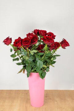 Close-up of a lot of red roses in a tin vase with handles on a wooden table on a neutral background. Vertical photo