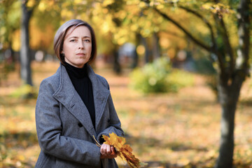 portrait of a beautiful woman with yellow leaves, posing in an autumn city park, she's in a sad mood