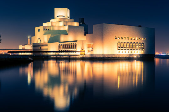 Doha, Qatar - Apr. 2020: Modern building in downtown Doha, Qatar. View at night. The building is lit with warm yellow light against a dark night sky.