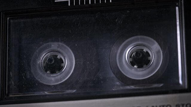 Audiocassette rotates in deck of old tape recorder. Transparent Audio cassette in retro player spinning and playing. Close-up. Retro call recording, playback, reel playing, vintage technology 80s, 90s