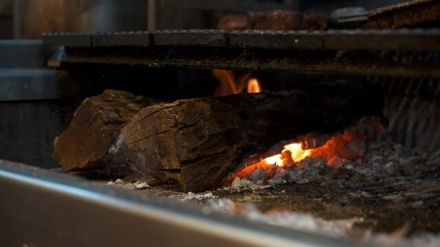 Logs smoke, embers glow, flames rise in wood burning grill, slow motion 4K