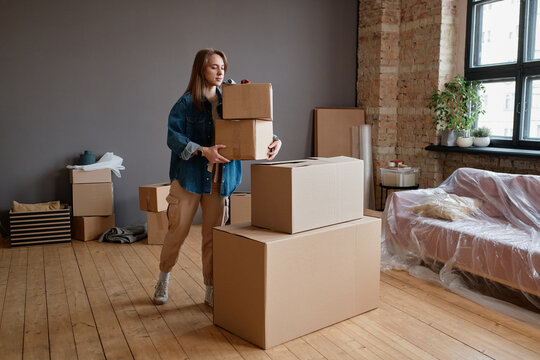 Horizontal shot of young woman moving to new apartment bringing and placing boxes with stuff in there