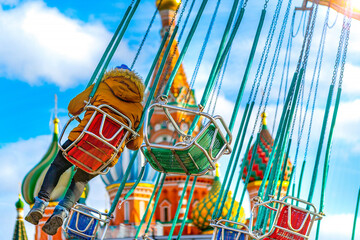 Armchairs of a flying carousel with a person in soft focus against the blue sky with clouds and sun...
