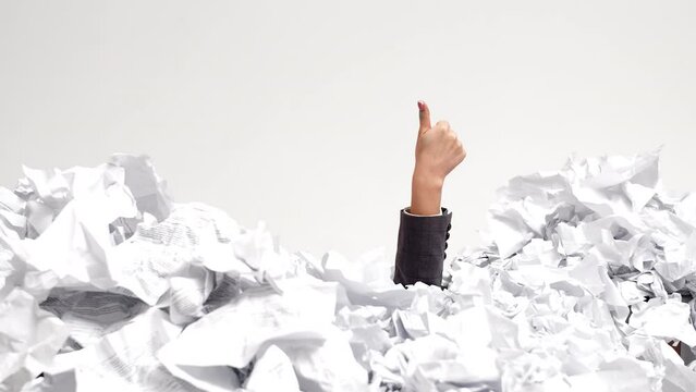 Female Office Workers Hand Sticks Out From Under Pile Of Crumpled Papers Making Like Gesture, Front View. Office Worker's Hand Sticks Out From Under Pile Of Crumpled Paper With His Thumb Up