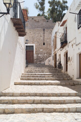 Fototapeta na wymiar Narrow street in the old town of Ibiza known as Dalt Vila. Black bicycle in an empty street in the old city. Stairs in a stone pedestrian street with old houses with white painted walls.