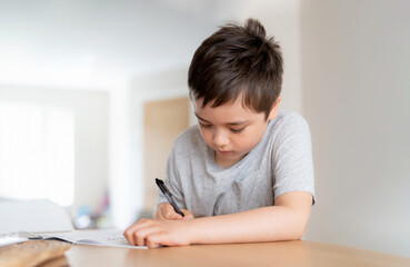 School kid using black pen drawing or writing the letter on paper, Young boy doing homework, Child with pen writing notes in paper sheet during the lesson.Cute pupil doing test, Homeschooling concept