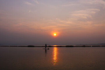 Asian woman playing surfboard in the river in the morning with beautiful sunrise.